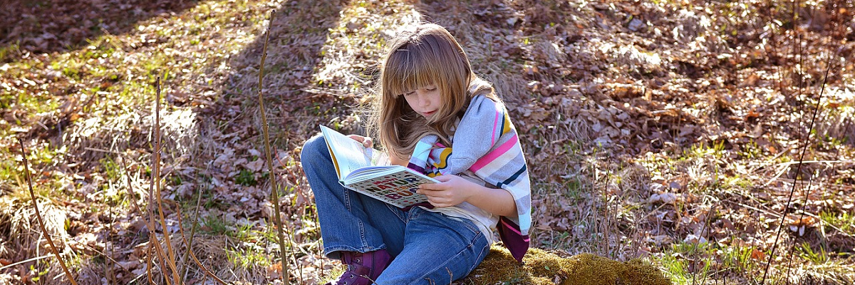 Lapsi lukee kirjaa ulkona.