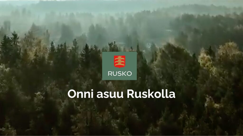 Metsäinen maisema Ruskolta ja Ruskon kunnan logo sekä slogan Onni asuu Ruskolla
