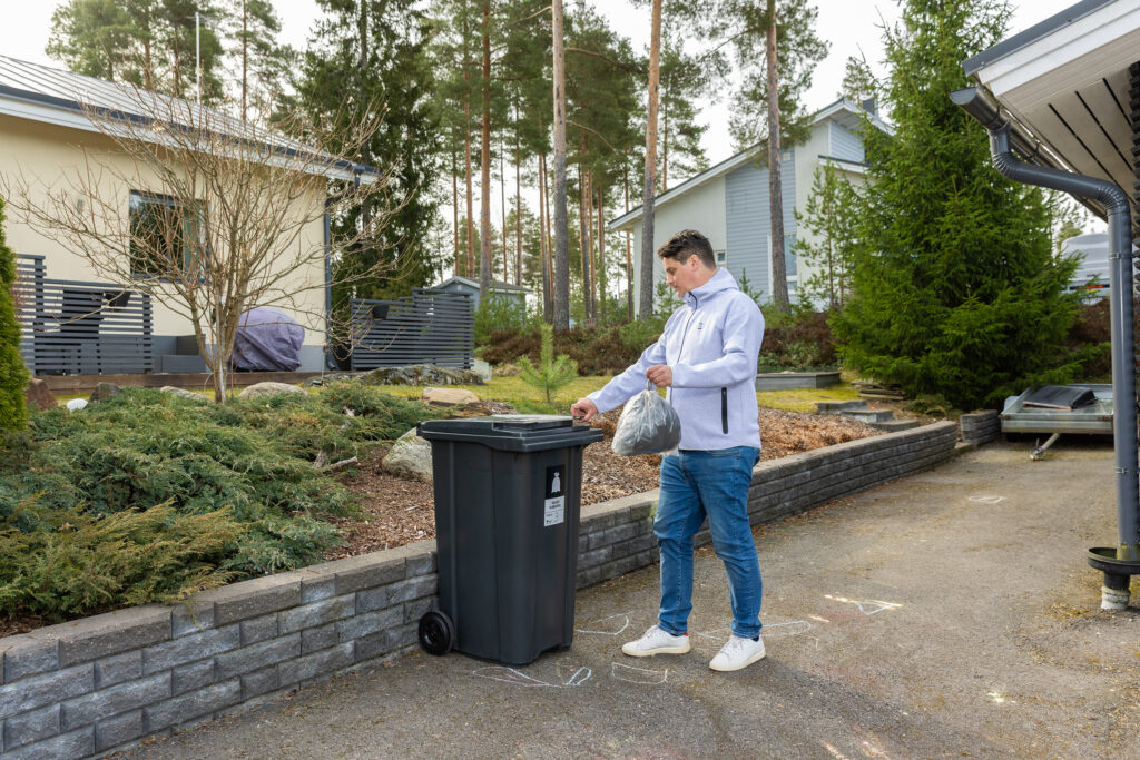 Mies vie roskapussia jäteastiaan omakotitaloalueella.
