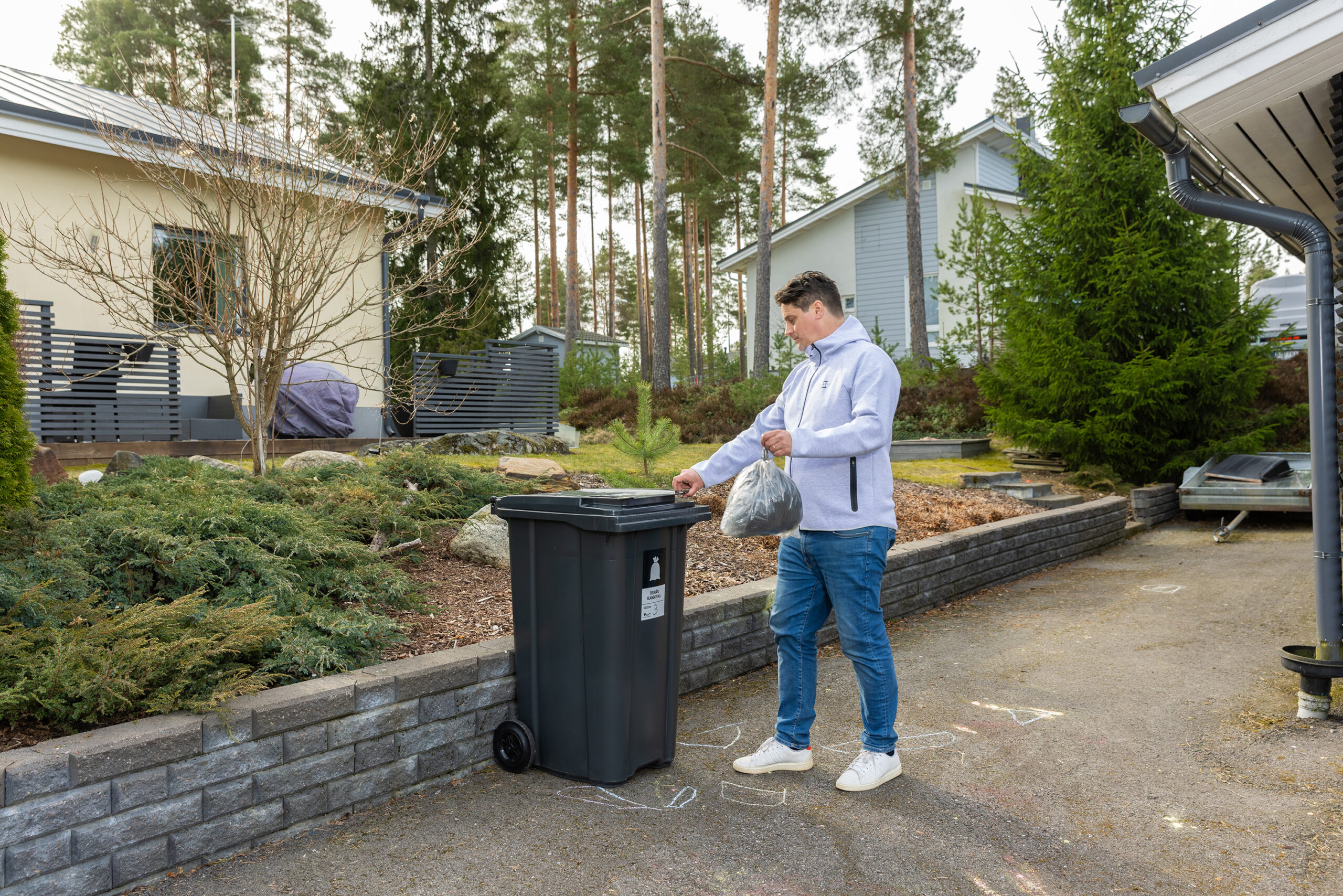 Mies vie roskapussia jäteastiaan omakotitaloalueella.